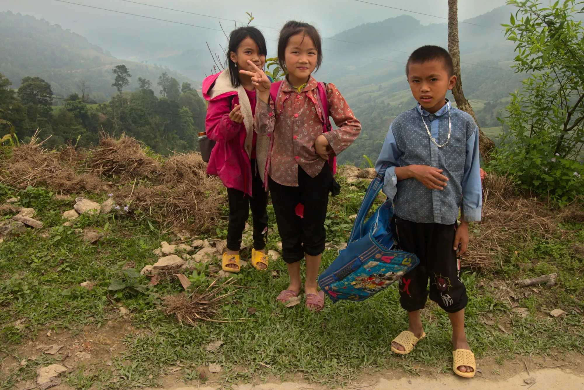 Ba em nhỏ trên sườn núi ở Lùng Vài, Hà Giang, phía sau là núi rừng mờ sương